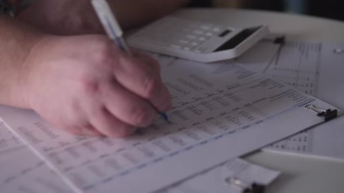 Hand Writes Financial Data with Calculator and Documents