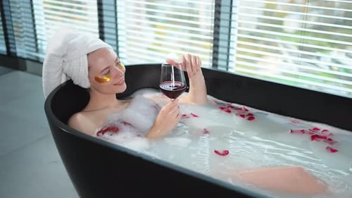 Spa Relaxation Woman Lying in Bath with Holding Glass with Red Wine Girl Relaxing in Bathroom at