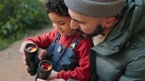 Un père apprend à son enfant à utiliser des jumelles à l'extérieur