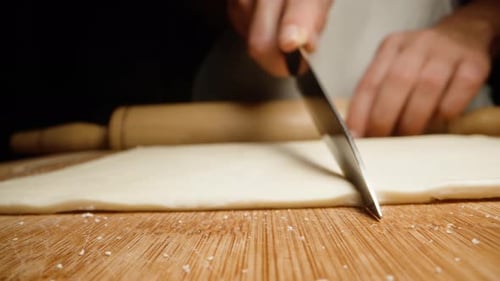Person Cutting Dough with a Knife on Wood
