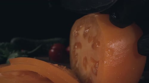 Chef cutting fresh yellow tomato with a knife on wooden cutting board