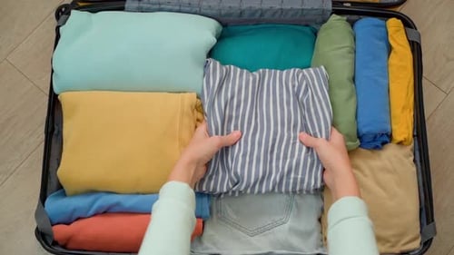 Top down view of a female traveler packing clothes in an open suitcase.