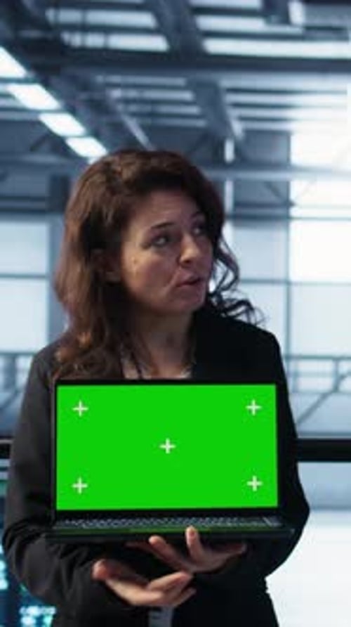 Woman Presents Laptop with Green Screen in Server Room