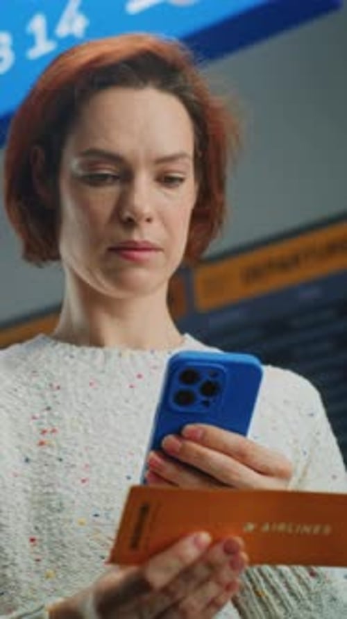Woman Checks Phone, Airport Flight Departure Board