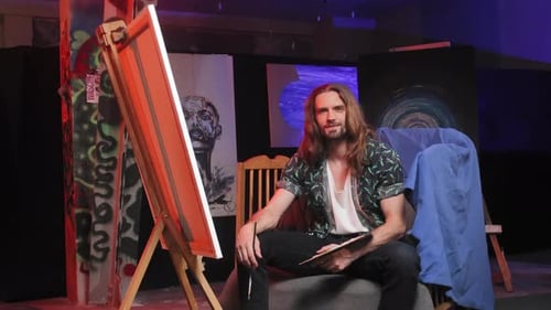 Illustrator Sitting Amidst Various Artworks Near Easels
