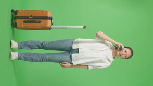 Asian Female Traveler With Luggage Talking On Smartphone While Standing In The Green Screen