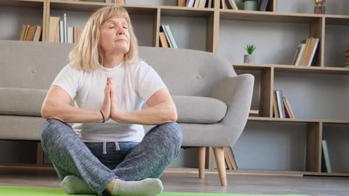 Senior Woman Meditating At Home on Yoga Mat