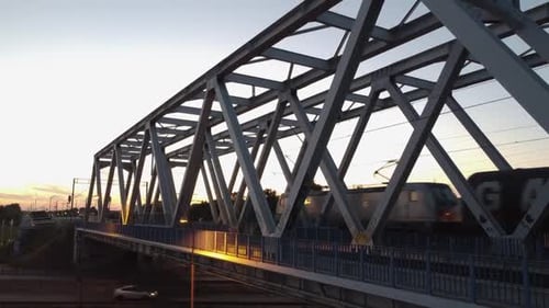 Aerial drone footage of a bridge while trains pass by on a sunset in Warsaw Poland with a city scape
