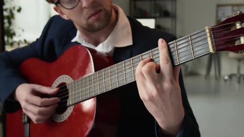 Section intermédiaire d'un jeune entrepreneur apprenant à jouer de la guitare acoustique pendant la journée de travail