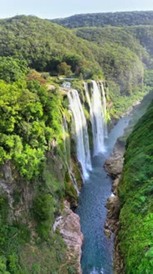 Aerial drone view of Tamul Waterfall cascading down green cliffs into a turquoise pool below. Vertic