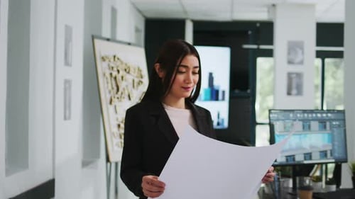 Asian Architect Studying Blueprint Papers in Creative Agency