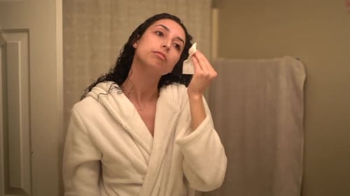 Woman Cleans Face with Cotton Pad in Bathroom