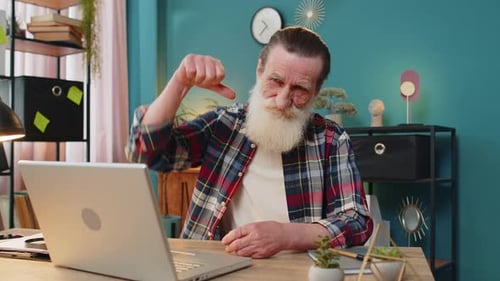 Senior Man Working on Laptop Computer at Home Office Showing Thumbs Down Sign Dislike Disapproval