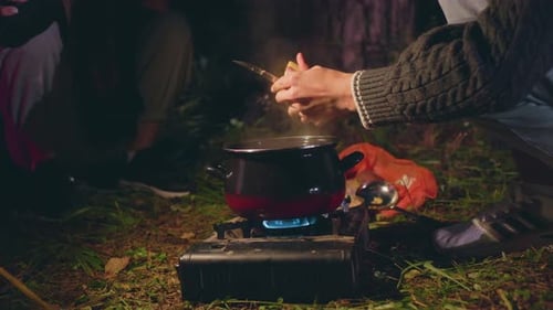 Close Up Of People Cooking Over Stove While One Uses Light During Camping