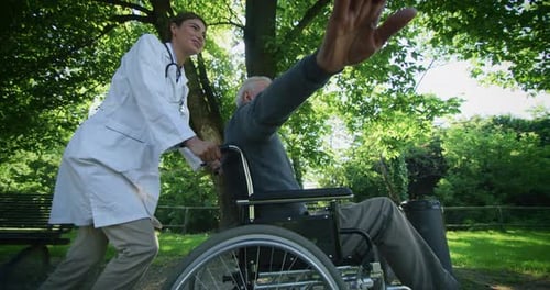 Slow motion of carefree and happy young woman social worker or nurse and senior man in a wheelchai