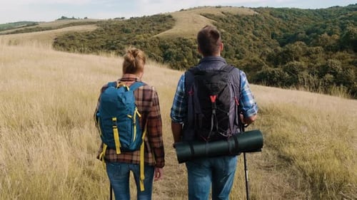 Rear view of couple with backpacks hiking together.