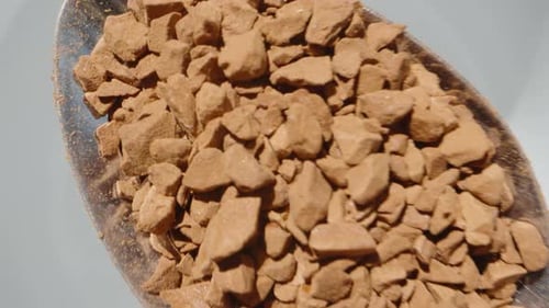 I pour instant coffee from a spoon into a white mug. Dolly slider extreme close-up.