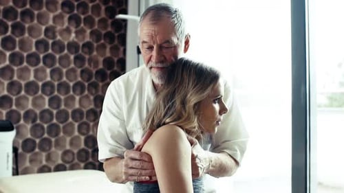Senior Man Massaging Young Woman's Shoulder Indoors