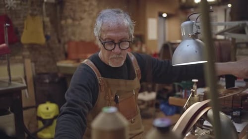 side view in slow motion of leather craftsman sitting while sewing leather belt