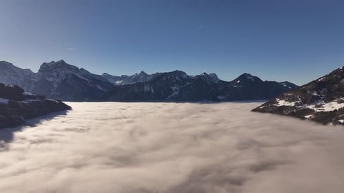 Drone flying above the clouds with mountain peaks in the background, partially veiled by mist, creat