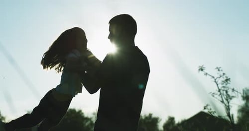 Silhouette of Father Holding Daughter in Sunny Field