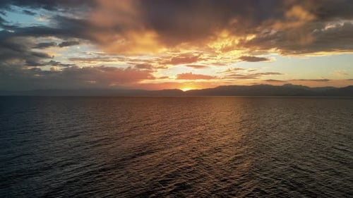 Luftbild über dem Meer bei lebhaftem Sonnenuntergang über dem Horizont mit orangefarbenen und gelben Wolken