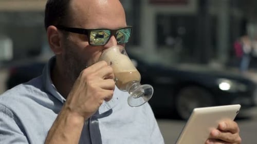 Man Using Tablet Computer And Drinking Coffee In Cafe In City