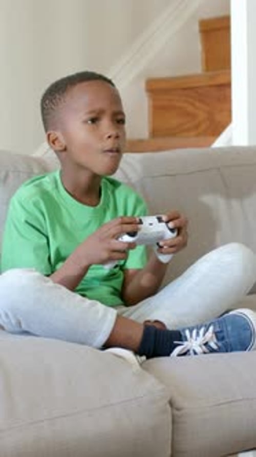 Vertikales Video: Spielender Junge, der zu Spielbeginn ein weißes Pad benutzt, sich zu Hause auf die Couch lehnt und ein grünes T-Shirt trägt