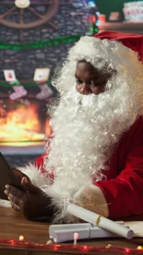 Vertical Video Santa Claus Uses a Tablet to Navigate Online Webpages in His North Pole Cabin