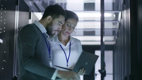 Male and Female Server Engineers Work on a Laptop in Data Center. He Opens Rack Server Cabinet.