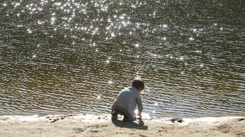 Little boy sitting on the beach at river and playing with sand