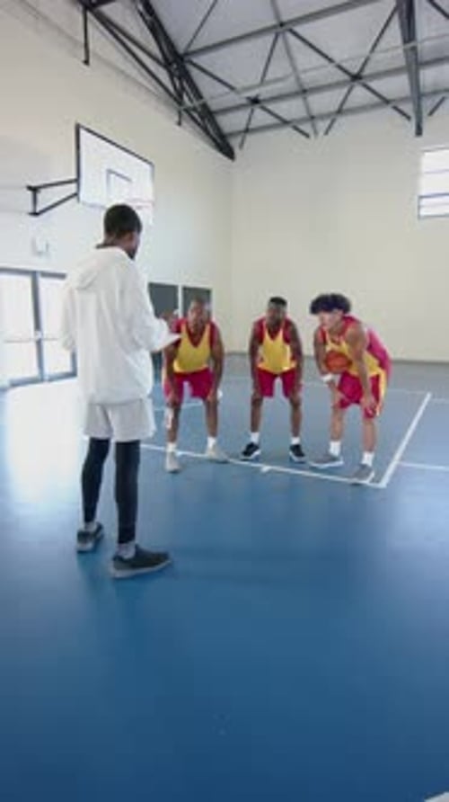 Vertical video: Basketball coach instructing male players on court during practice session