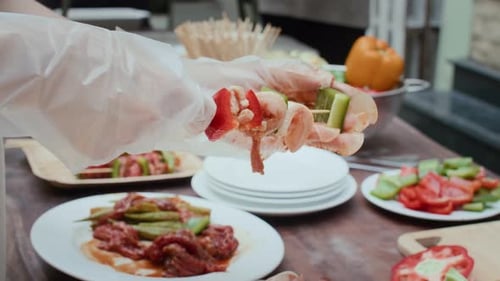 Gloved Hands Putting Food on Wooden Skewer