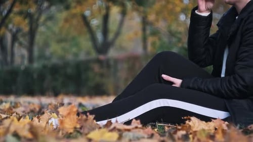 Young Woman Enjoy Coffee on Grass in Autumn Park Among Fallen Yellow Leaves