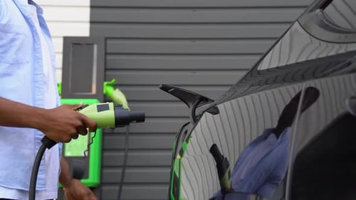 Unrecognizable Black Man Unplugs Charging Cable Electric Vehicle at Station Green Energy Eco