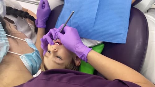 A Doctor Dentist in a Medical Mask and Purple Rubber Gloves Puts a Seal on a Little Boy Toddler