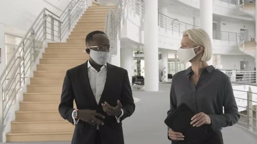 Business people wearing face mask meeting in modern corporate office lobby and walking