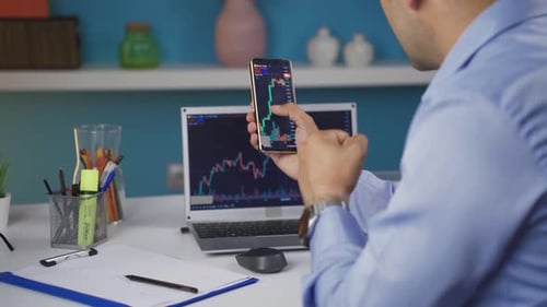 Young Adult Analyzing Charts on Phone and Laptop