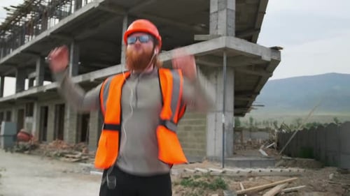 Engenheiro construtor barbudo com óculos escuros dançando no canteiro de obras, pulando e comemorando