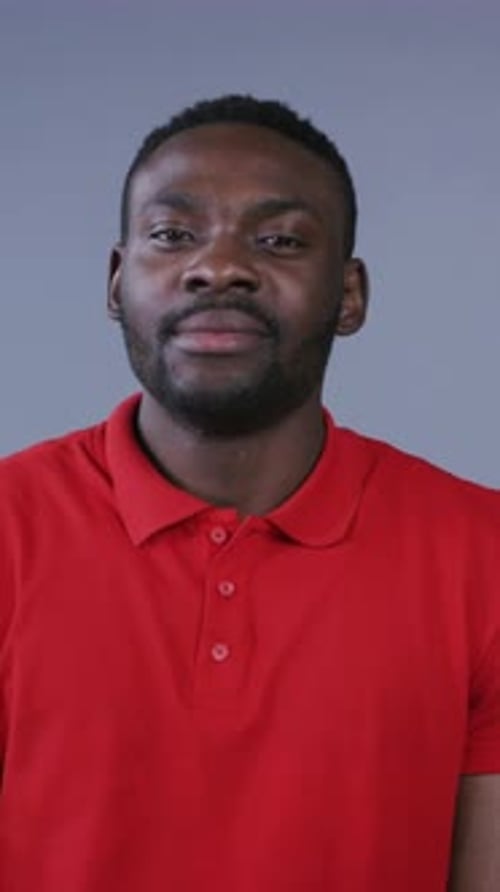 Attractive AfroAmerican Man in Stylish Red Tshirt Joyfully Smiles Straight to Camera on Gray