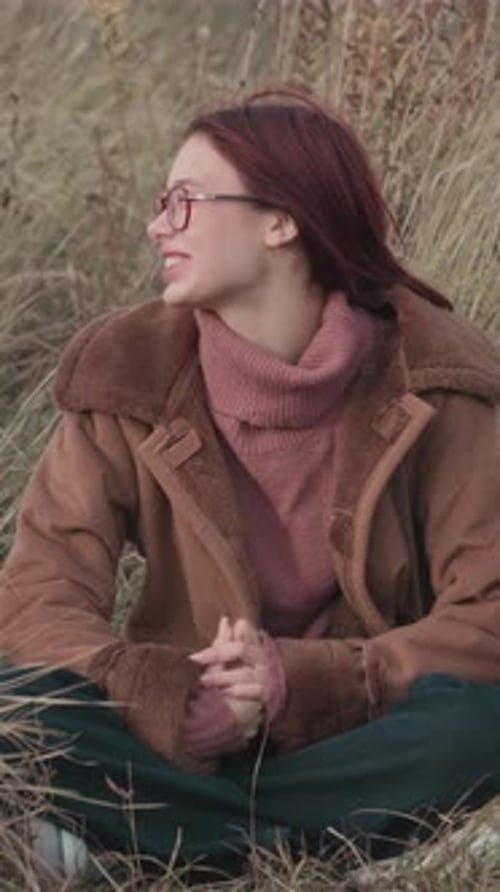 Smiling teenage girl in pink sweater and brown shearling coat having a joyful conversation outdoors.