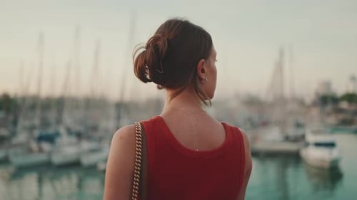Close-up, girl stands on the seashore and looks at the harbor with yachts