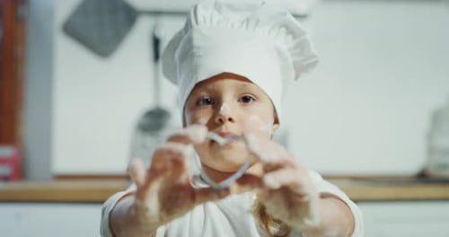 Portrait of a beautiful kid (girl) dressed as a chef while showing a form in the shape of a heart.