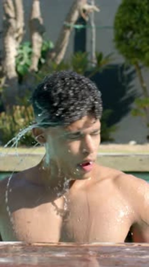 Vertical video: Rising from pool, shirtless man shaking head to remove water at home pool, wet hair