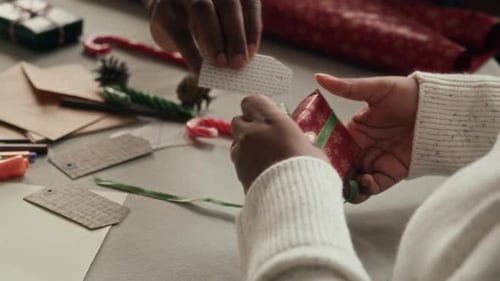 Hands Tying Ribbon on Christmas Present at Table