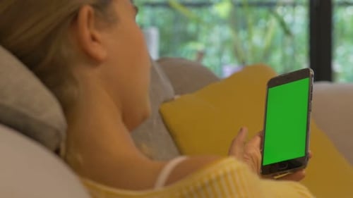 Close-up woman holding smartphone green screen while chilling on the Couch