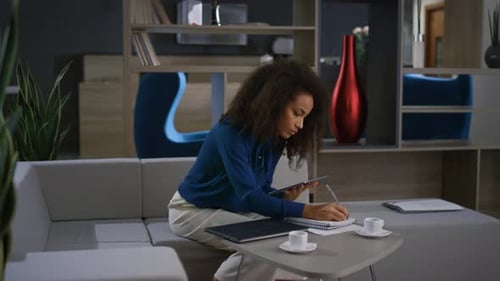 Woman Uses Tablet, Writes in Notebook in Office