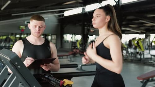 Woman Exercising on Treadmill with Trainer in Gym