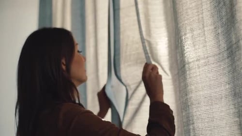 Woman Opens Curtains to Bright Sunlight in Room