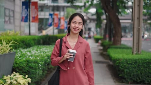 Young Asian Businesswoman Walking and Holding a Coffee on a City Street